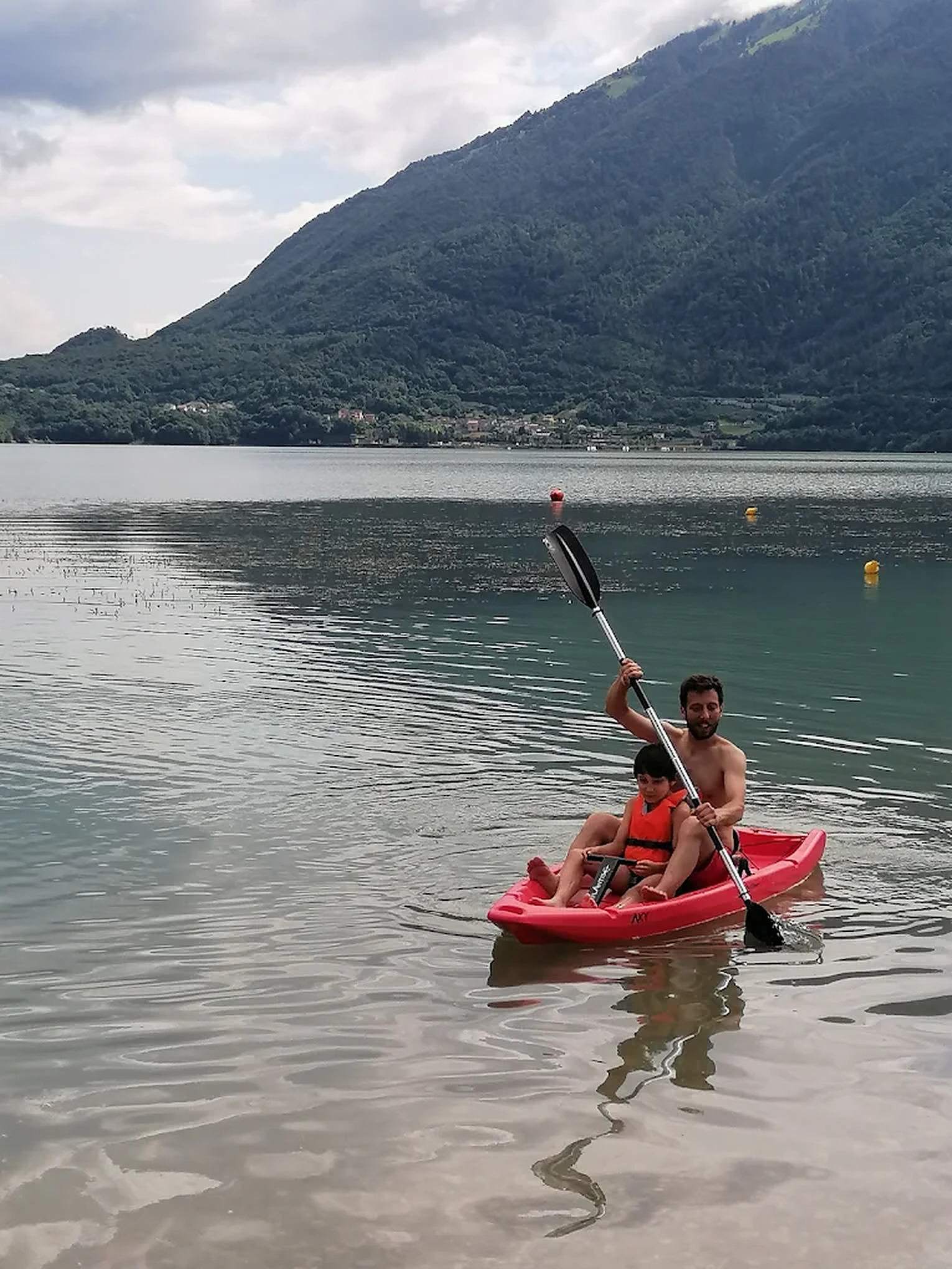 Papà e bambino in kayak sul Lago di Santa Croce, con le montagne dell'Alpago sullo sfondo